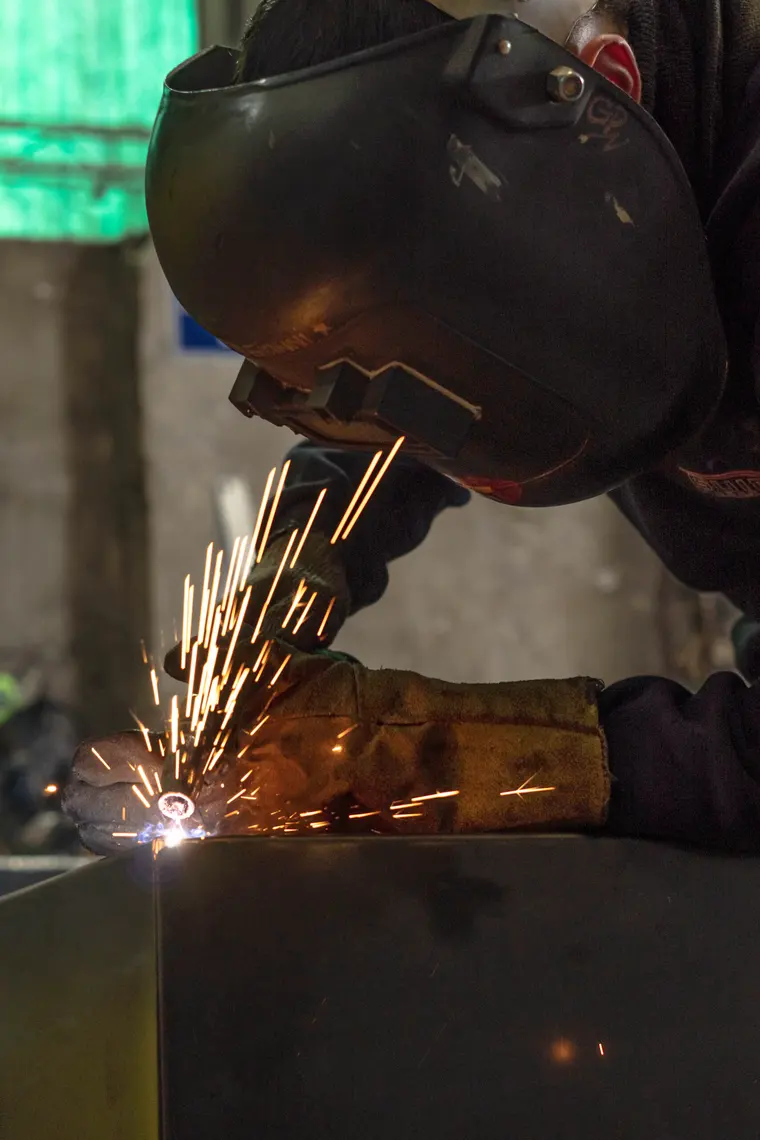 Welder in a mask, sparks over a sheet metal part