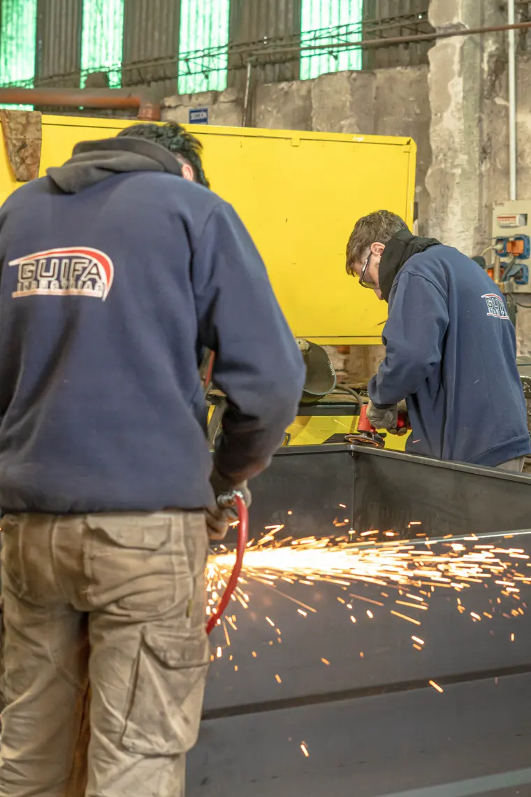 Two workers in Guifa sweatshirts grinding a structure