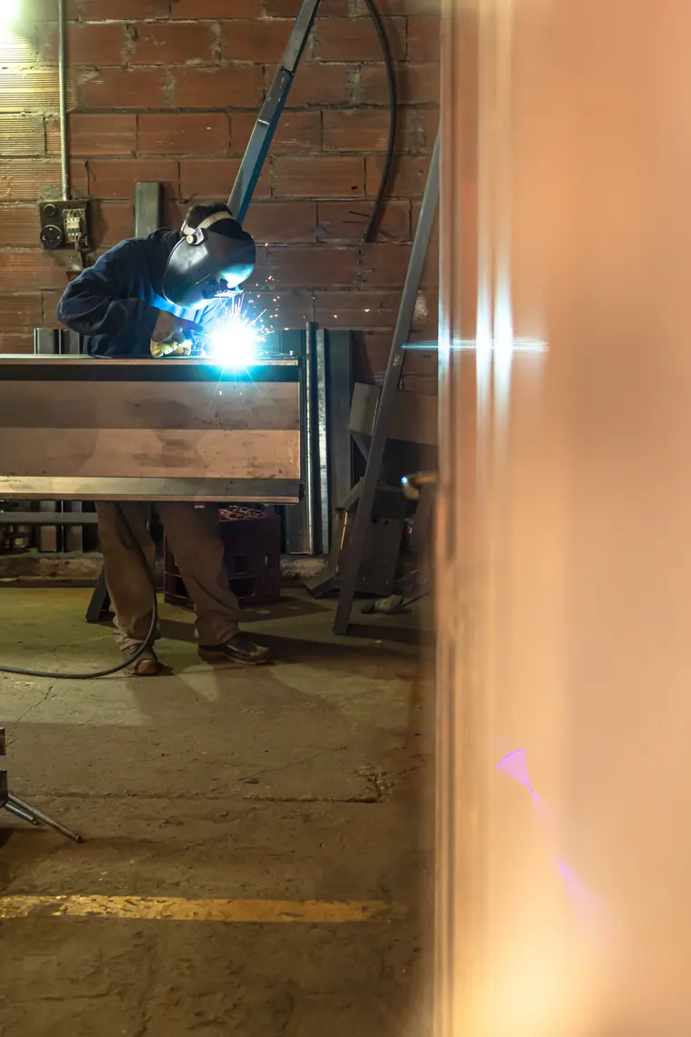 Welder working at the back of the shed, among steel sheets