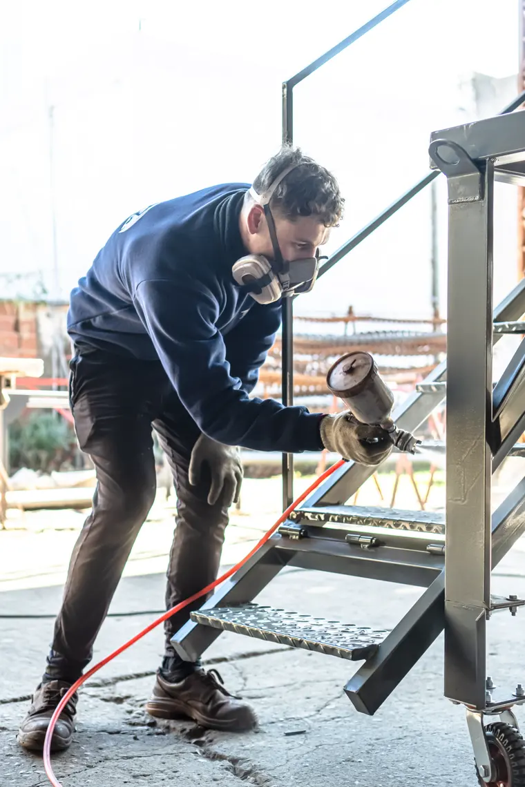 Worker in a mask grinding a metal staircase outdoors